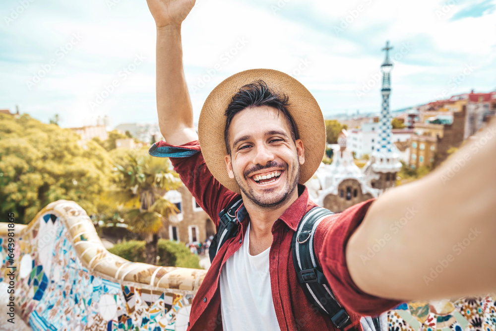 Happy tourist take selfie self-portrait with smartphone in Park Guell, Barcelona, Spain - Smiling man on vacation looking at camera - Holidays and travel concept - obrazy, fototapety, plakaty 