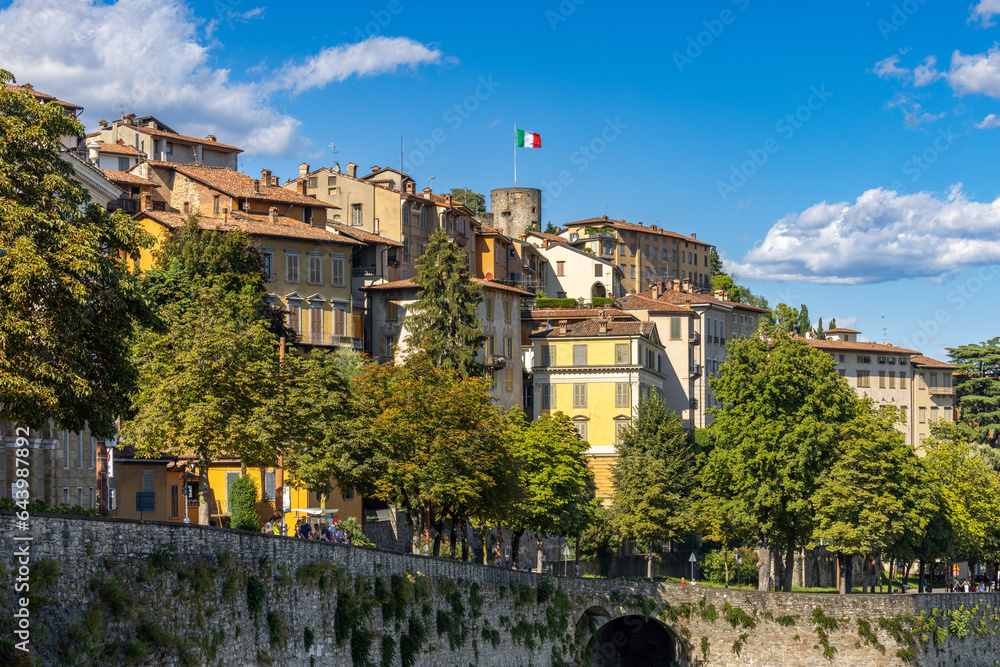 Bergamo, Italy, August 7, 2023; View of old buildings on the cliff with a flag of Italy against blue sky
