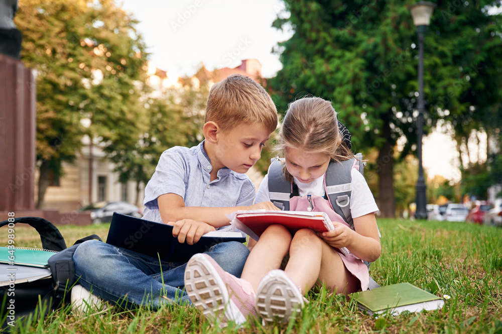 Sitting on the green grass. Young school children of boy and girl are together outdoors Sitting on the green grass. Young school children of boy and girl are together outdoors