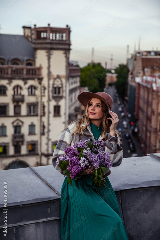 Fototapeta premium Beautiful girl with lilacs on the roof at sunset in summer