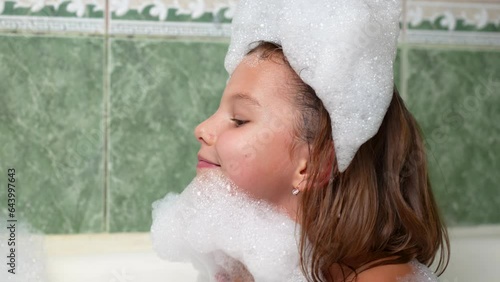 Cute girl playing with soap foam in the bath photo