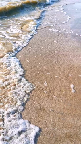 Foamy sea waves wash the sandy beach on a sunny summer day. vertical video.