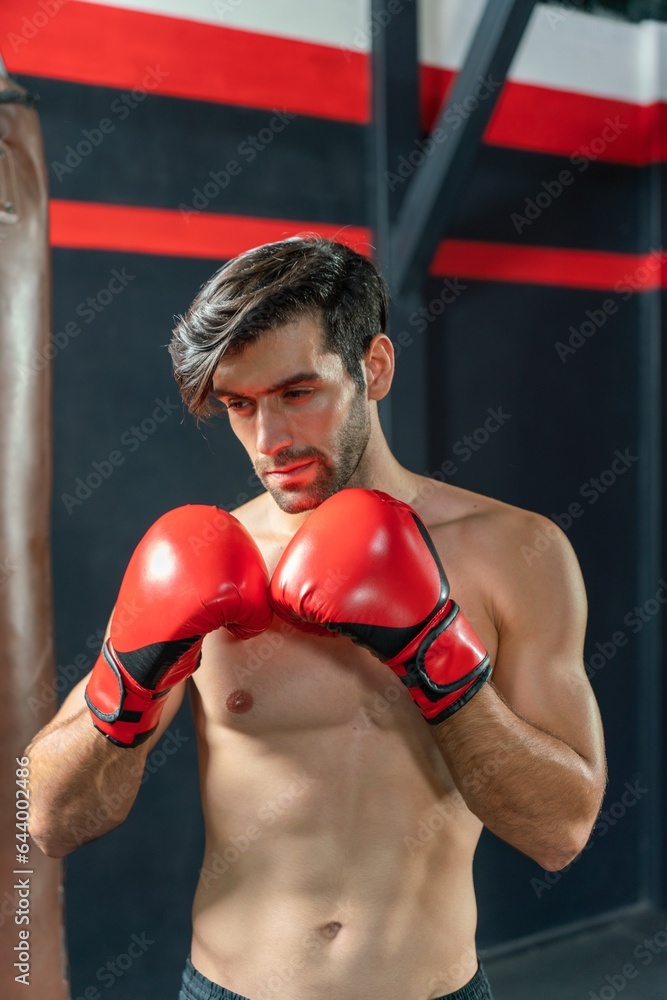 Handsome Middle Eastern man with a muscular body physique showing how to throws powerful punches at a punching bag, displaying his boxing prowess in a boxing gym Handsome Middle Eastern man with a muscular body physique showing how to throws powerful punches at a punching bag, displaying his boxing prowess in a boxing gym