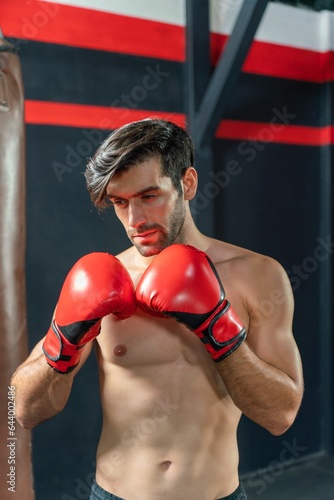 Handsome Middle Eastern man with a muscular body physique showing how to throws powerful punches at a punching bag, displaying his boxing prowess in a boxing gym