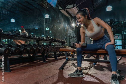 Determined young Asian woman strengthens her arm with single-arm dumbbell rows on the bench press, showing her dedication to building muscle at the gym