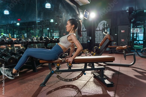 Young Asian woman dedicates herself to leg stretching exercises on the bench press, highlighting her commitment to flexibility and fitness in the gym