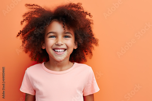 Portrait of a smiling, happy young girl with an afro, wearing a pink T-shirt, on an orange background © Lucy Welch