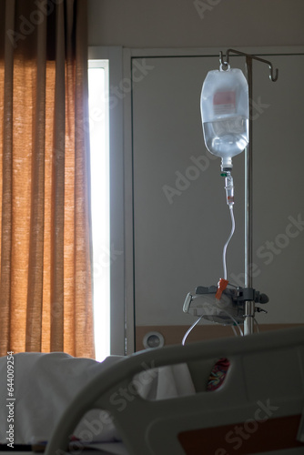 A stand with drip bag beside the bed at hospital. The saline solution drip for patient at hospital room.