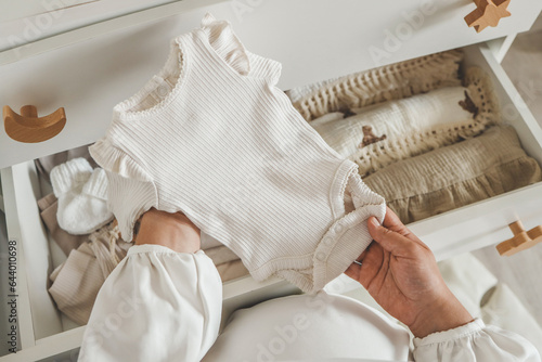 A pregnant woman holds a beige bodysuit in her hands, the concept of expecting a baby