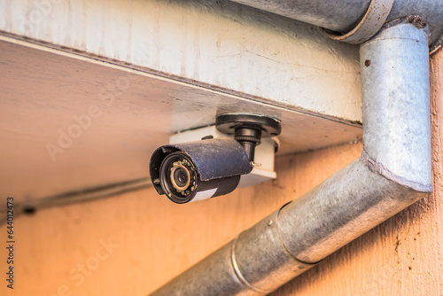 Fototapeta Naklejka Na Ścianę i Meble -  Video camera suspended from the roof of a private house on the street. Security of a private house with a camera. A small camera for the protection of the yard.