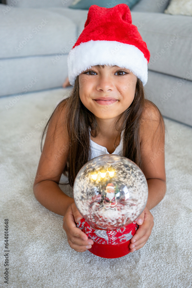 Happy little girl whit Santa hat sitting at home and looking at camera Happy little girl whit Santa hat sitting at home and looking at camera