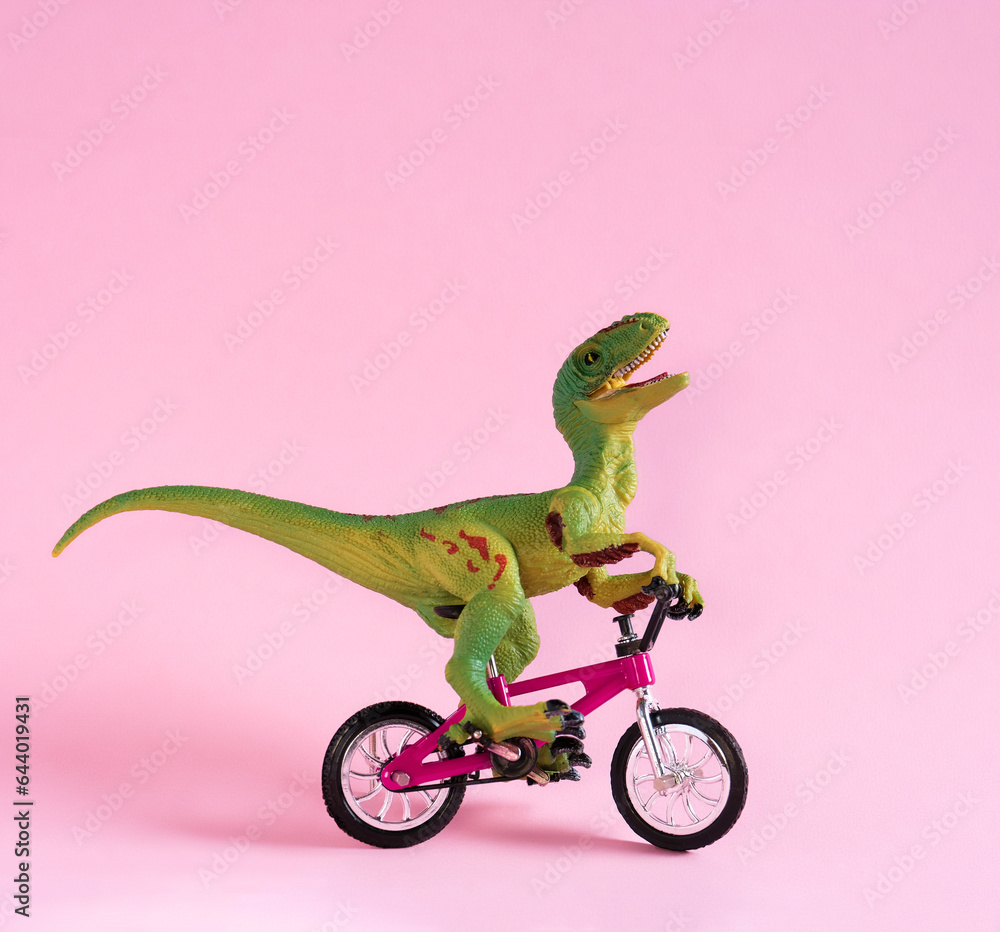 Fototapeta premium Cute happy dinosaur toy riding bicycle on pastel pink background. Cute eco friendly transport concept card.