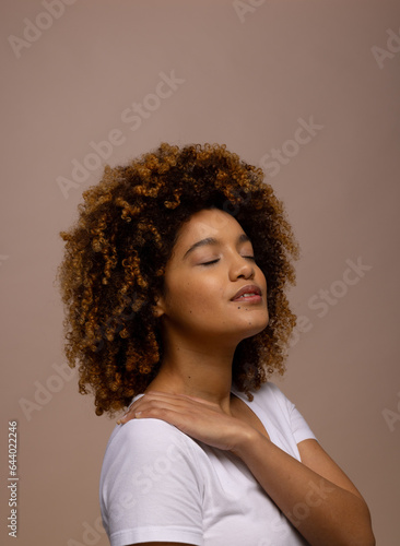 Biracial woman with dark curly hair, with hand on shoulder and closed eyes, copy space
