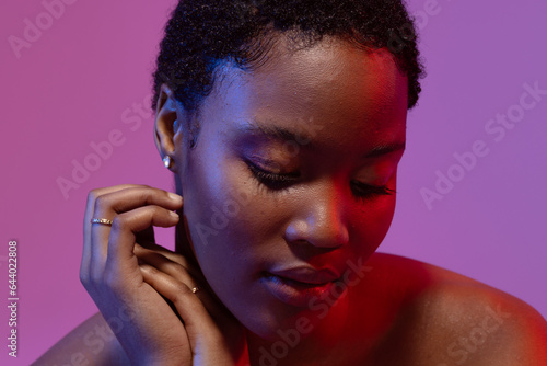 African american woman with short hair looking down and touching hands on purple background © wavebreak3