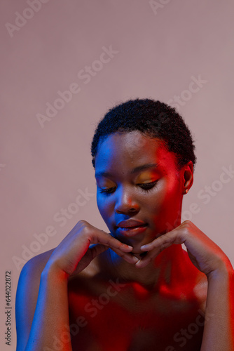 African american woman with short hair with hands under chin in blue and red light, copy space