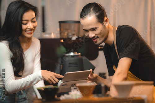 Asian Cashier is making order on touch screen of computer in cafe or store. Barista is using the screen to receive orders from customers who are pointing to order coffee.