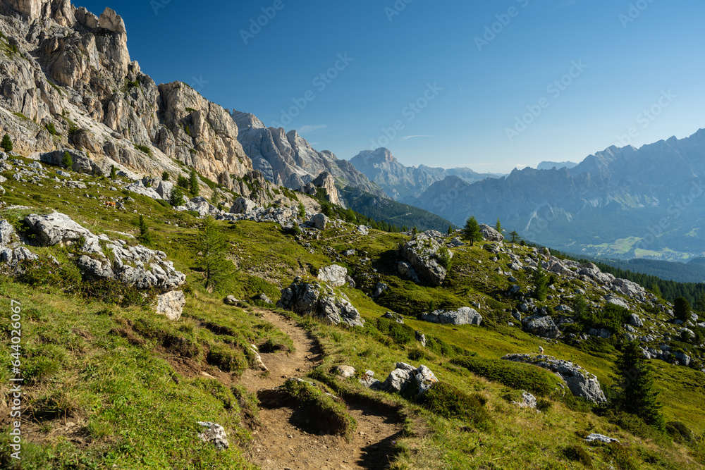 Trail from Pass Giau to Cinque Torri in the Dolomites Mountains with green grass and mountains in the background in the summer at cloudless sky and warm day