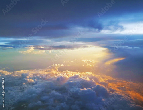 Fototapeta Naklejka Na Ścianę i Meble -  Stunning arial view of Golden sunrays and rays of sunlight over the clouds on the blue sky background looking out of aircraft window. Scenic view above the clouds