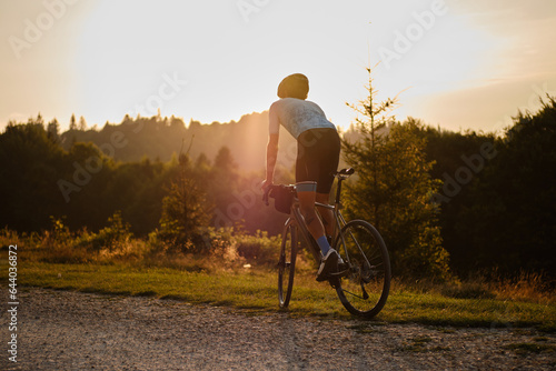 A fit male cyclist practicing on a gravel road at sunset. He is riding a gravel bike with a view of the mountains. Bucegi Mountains, Romania photo