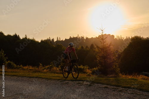 Woman cyclist is riding a gravel bike on a gravel road at sunset with a view of the mountains.Empty mountain road. Cycling gravel adventure in Romania. Bucegi Natural Park.