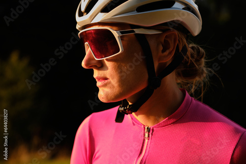 Fototapeta Naklejka Na Ścianę i Meble -  Portrait of female cyclist in white helmet, sunglasses and pink jersey. Healthy and active lifestyle concept.Close-up portrait of woman athlete. Cycling life.