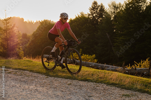 Woman cyclist is riding a gravel bike on a gravel road  at sunset with a view of the mountains.Empty mountain road. Cycling gravel adventure in Romania. Bucegi Natural Park. © Ketrin
