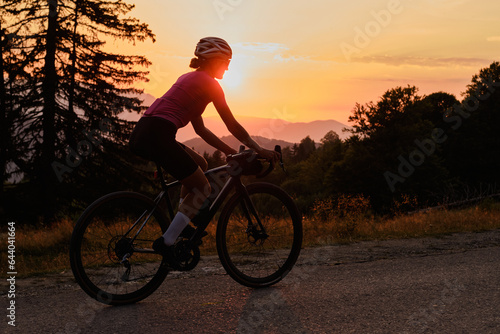 Woman cyclist is riding a gravel bike on a gravel road at sunset with a view of the mountains.Empty mountain road. Cycling gravel adventure in Romania. Bucegi Natural Park.