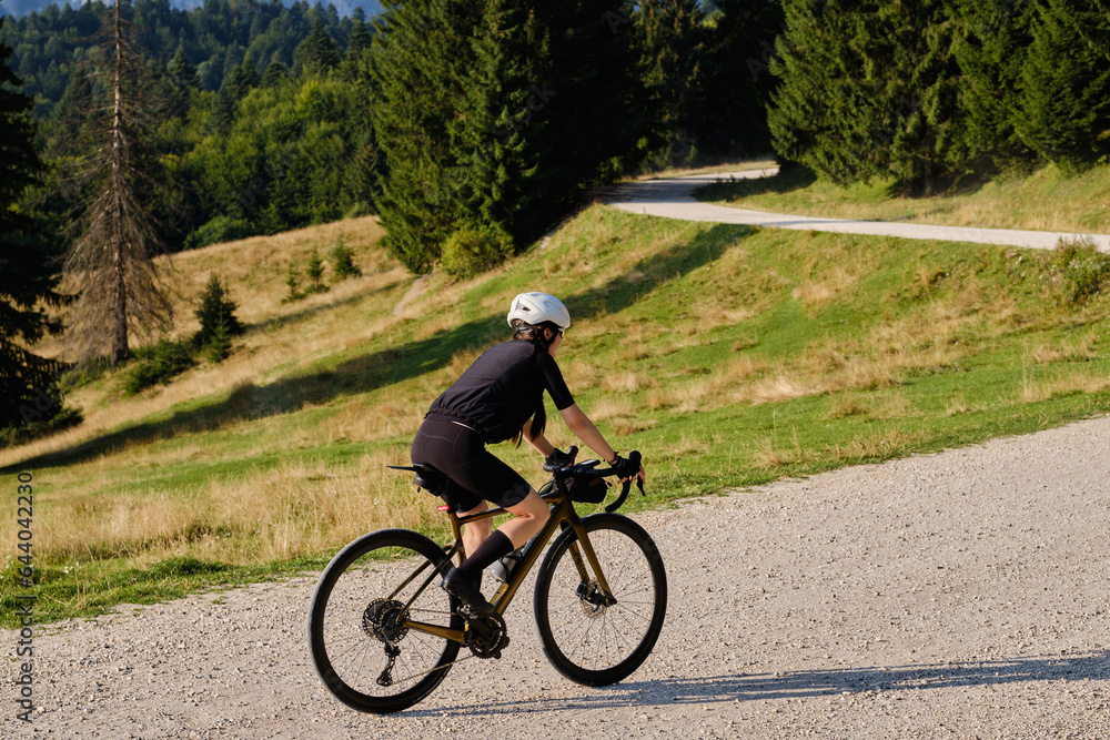 Fototapeta premium Female cyclist is riding on a gravel road with a mountain view. The athlete is wearing full cycling gear and training for a cycling competition. Cycling gravel adventure in Romania.Bucegi Natural Park