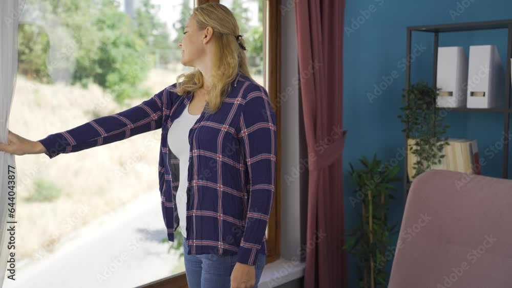 The woman opens the closed curtains in her house. The woman opens the closed curtains in her house.