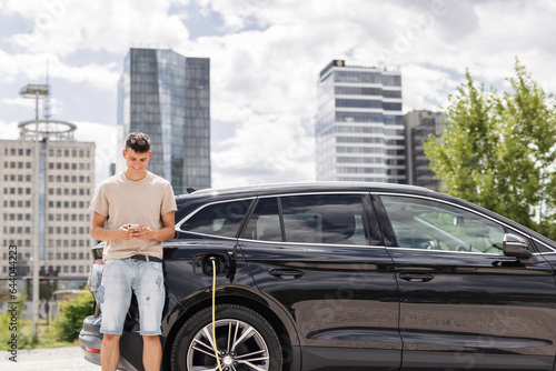 Men charging electric car in city and adjusting EV charging app on smartphone © 24K-Production