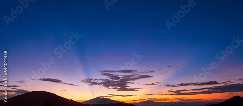 Dramatic evening sky background over silhouette mountains with majestic yellow sunlight and dark clouds on dark blue twilight in panoramic view