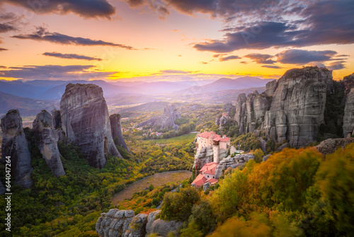 Panoramic landscape of Meteora, Greece at romantic sundown time with real sun and sunset sky. Meteora - incredible sandstone rock formations.  The Meteora area is on UNESCO World Heritage. photo