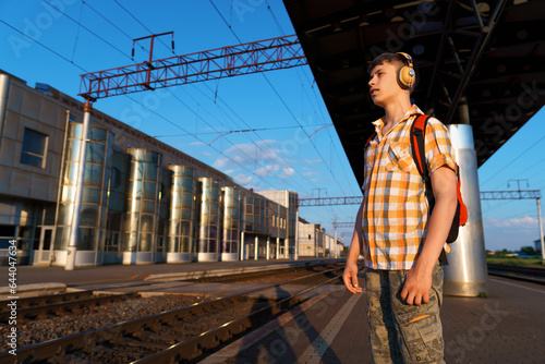 a student poses at a railway station, a teenage boy walks along the platform to the train, he has a backpack and books, goes to study, the concept of education