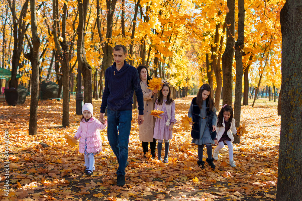 Naklejka premium portrait of a family with children in an autumn city park, happy people walking together, playing with yellow leaves, beautiful nature, bright sunny day