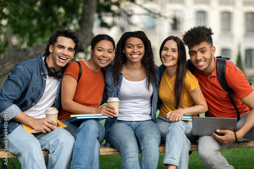 Outdoor Portrait Of Happy Young Multiethnic Students Relaxing On Bench At Campus
