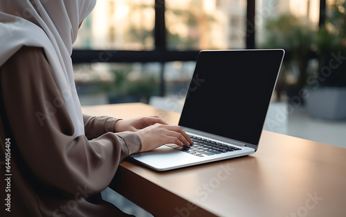 Fotografia Unrecognizable arab woman in hijab using laptop blank screen in coworking space