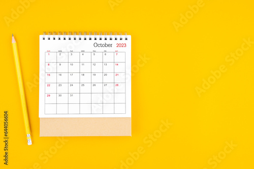 October 2023 desk calendar and wooden pencil on yellow color background. Time planning, day counting and holidays.