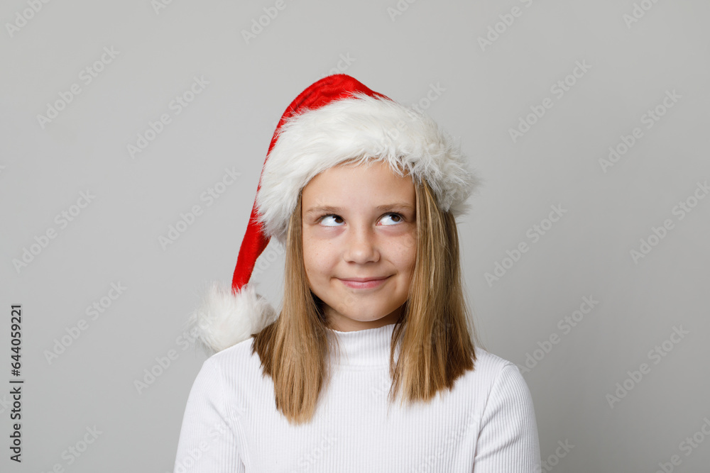 Cute mischievous child girl in Santa hat looking up on white background Cute mischievous child girl in Santa hat looking up on white background