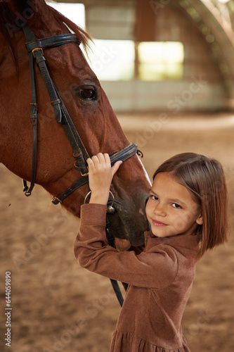 Embracing the animal. Cute little girl is with horse indoors