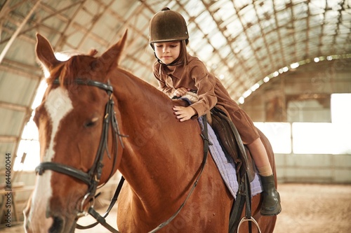 Riding the animal. Cute little girl is with horse indoors © standret