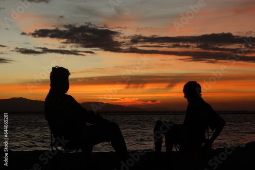 Silhouette of two young men standing by the lake enjoying the sunset. peaceful atmosphere in nature 