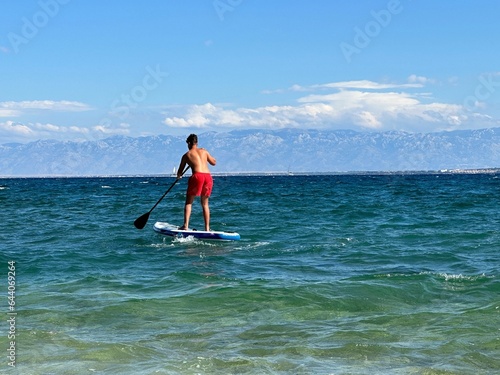 A man floats on a surfboard. Concept: Water sports, entertainment at sea. A young guy stands on a surfboard in the sea. © Сергій Колесніков