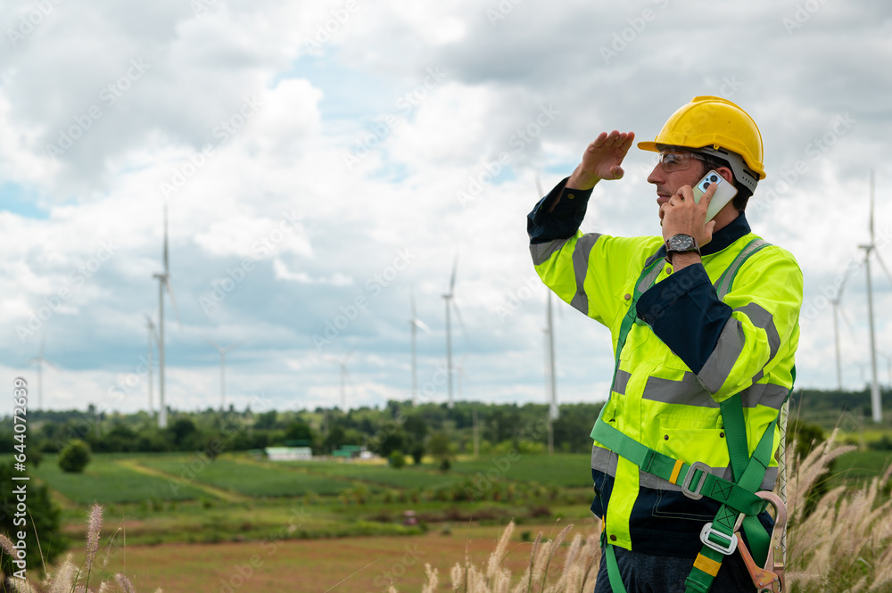 A smart engineer with protective helmet on head, using smartphone at electrical turbines field A smart engineer with protective helmet on head, using smartphone at electrical turbines field