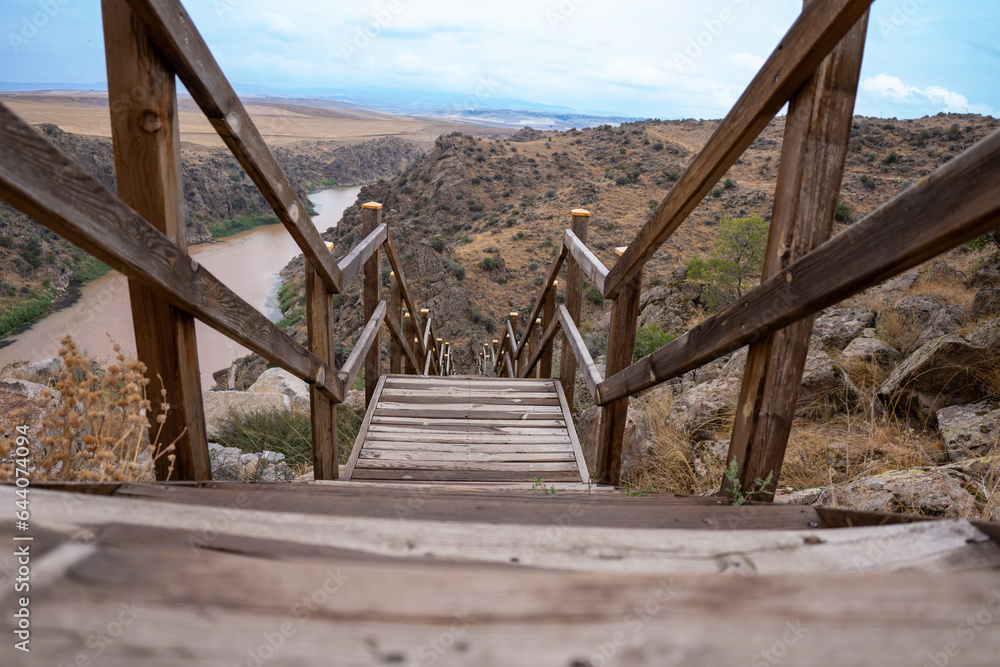 Wooden railing stairs descending from cliff to river Wooden railing stairs descending from cliff to river