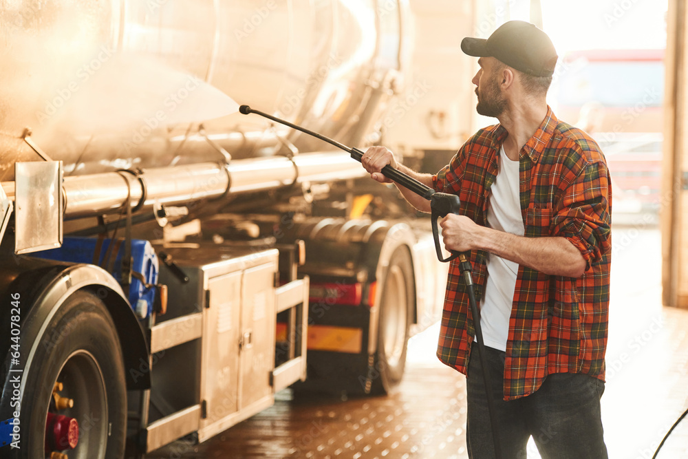 Washing the vehicle. Young truck driver in casual clothes Washing the vehicle. Young truck driver in casual clothes