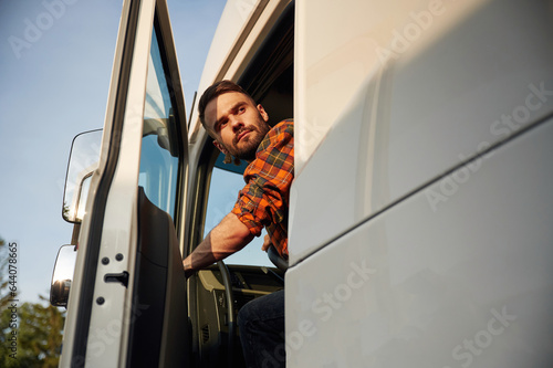 Looking through the door, sitting inside. Young truck driver in casual clothes photo