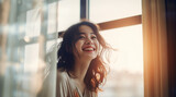 明るく美しいボケの、朝の陽ざしが入る窓辺で優しく笑う20代のアジア人女性