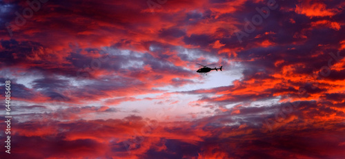Helecopter Flying at Sunset or Sunrise in Sky Dramatic Clouds with Mountains
