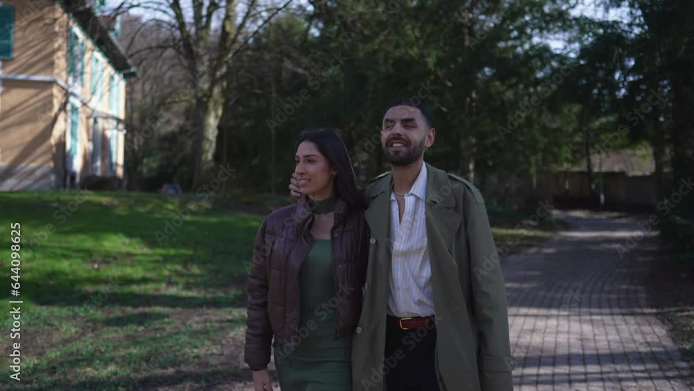 A Happy Middle Eastern couple walking outside at park during sunny day. Man pointing at distance with hand A Happy Middle Eastern couple walking outside at park during sunny day. Man pointing at distance with hand