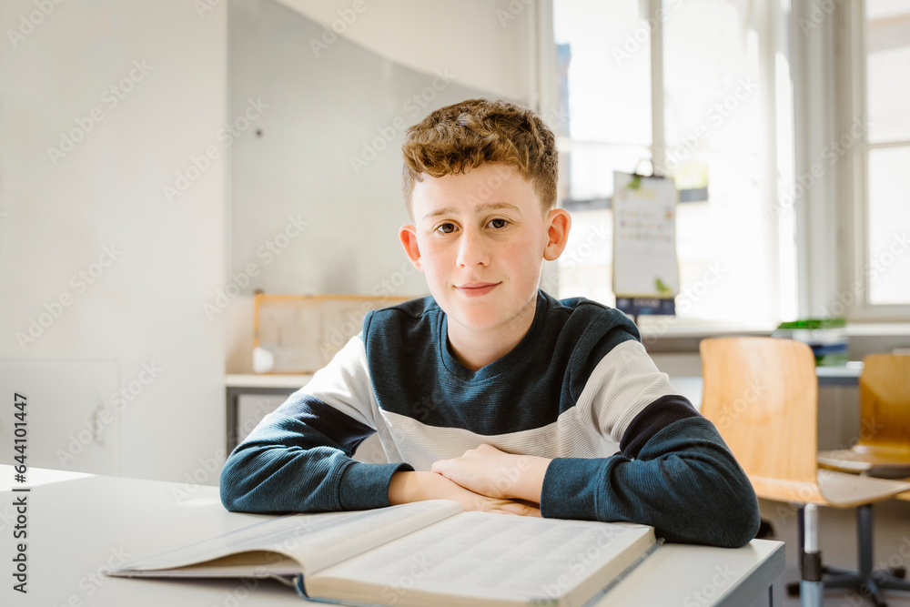 Portrait of schoolboy sitting with book at desk in classroom Portrait of schoolboy sitting with book at desk in classroom